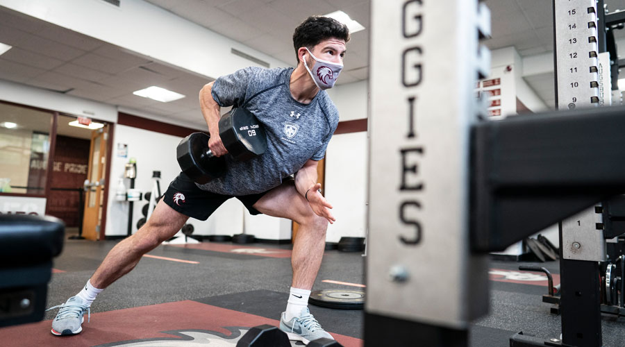 Mens Soccer player lifting in the weight room with a mask on